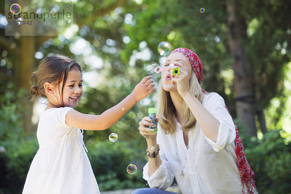 Mutter und ein kleines Mädchen beim Spielen mit dem Blasenstab im Freien