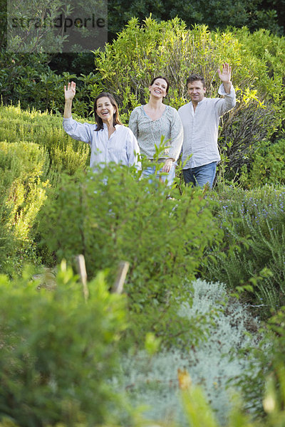 Ein reifes Paar  das mit seiner Mutter spazieren geht und mit der Hand im Garten winkt