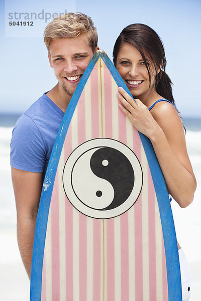 Portrait eines am Strand stehenden Paares mit Surfbrett