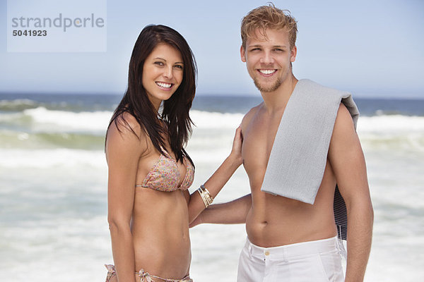 Porträt eines fröhlichen jungen Paares am Strand stehend