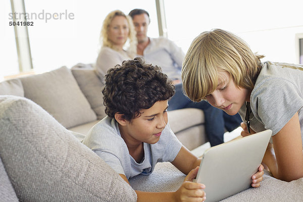 Brüder  die ein digitales Tablett benutzen  während ihre Eltern sie anschauen.