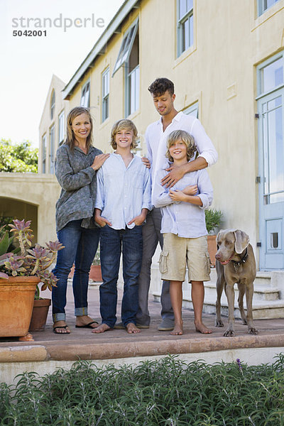 Porträt einer Familie  die mit ihrem Hund vor dem Haus steht.