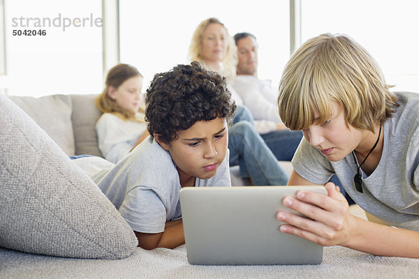 Teenager-Junge mit einem digitalen Tablett mit seinem Bruder und seiner Familie im Hintergrund