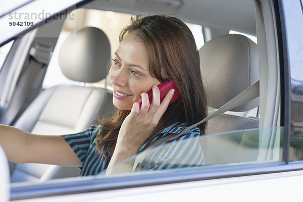 Schöne junge Frau  die beim Autofahren über das Handy spricht.