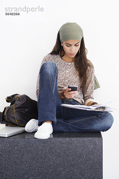 Schöne Frau mit dem Handy beim Lesen von Büchern vor weißem Hintergrund