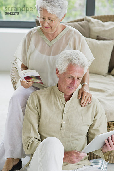 Ein älterer Mann arbeitet an einem digitalen Tablett und seine Frau liest eine Zeitschrift.