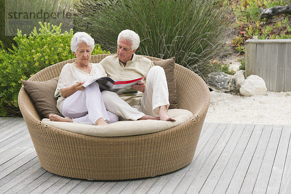 Seniorenpaar sitzt auf einer Weidencouch und liest eine Zeitschrift.