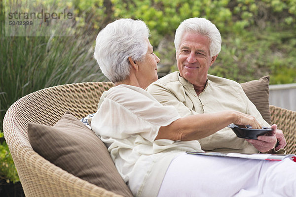 Seniorenpaar sitzt auf einer Weidencouch und isst Essen.
