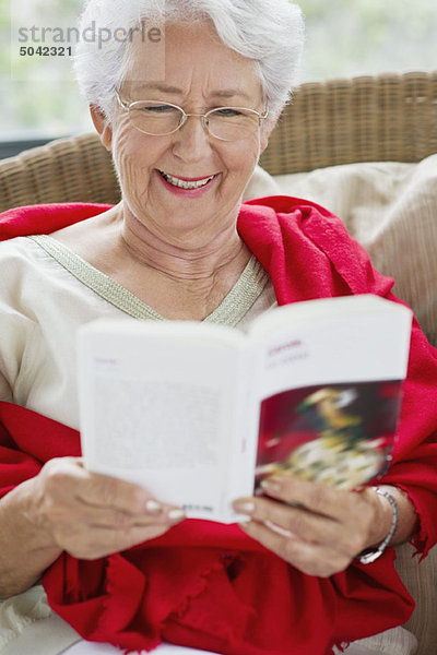 Seniorin liest eine Zeitschrift und lächelt