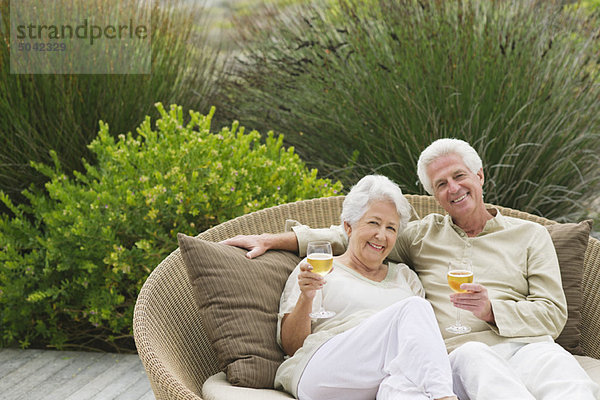 Seniorenpaar sitzt in einer Weidencouch und hält Weingläser.