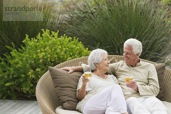 Seniorenpaar sitzend auf einer Weidencouch und lächelnd