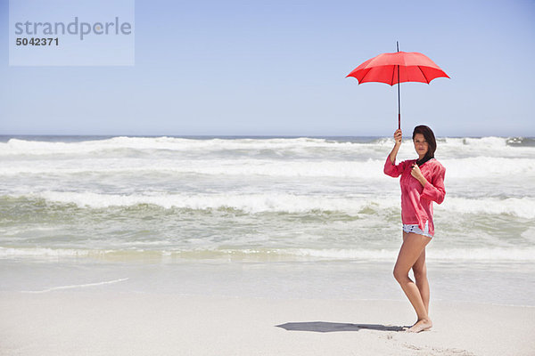 Frau am Strand stehend mit Schirm