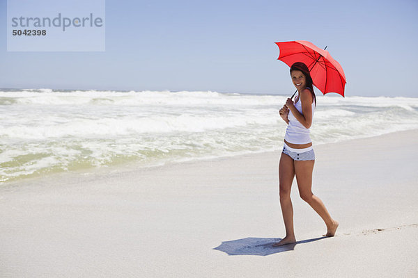 Frau  die mit einem Regenschirm am Strand spazieren geht.