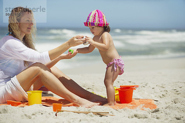 Frau und Tochter beim Spielen mit Eimer und Schaufel am Strand