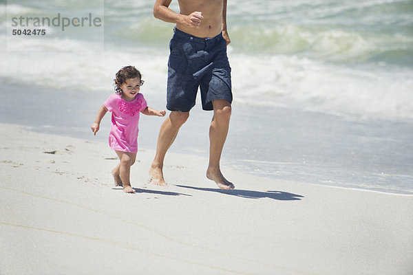 Mann läuft mit kleiner Tochter am Strand.