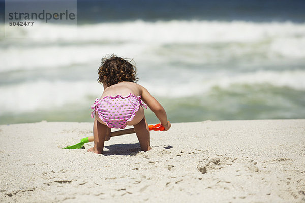 Rückansicht eines Mädchens  das mit einer Sandschaufel am Strand gräbt.