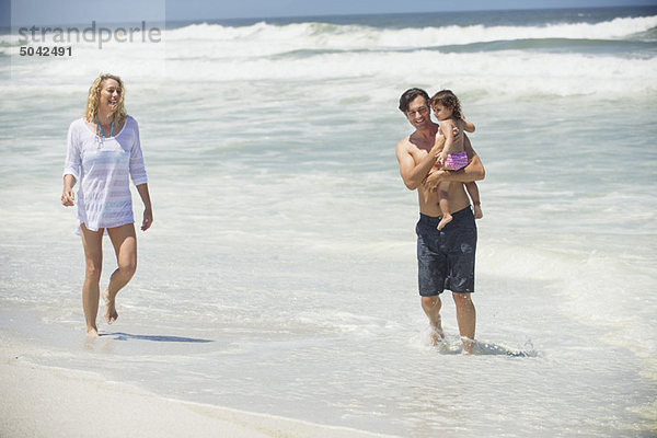 Ein Paar  das mit seiner Tochter am Strand spazieren geht.