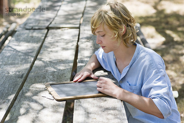 Seitenprofil eines kleinen Jungen beim Schreiben auf Schiefer im Freien