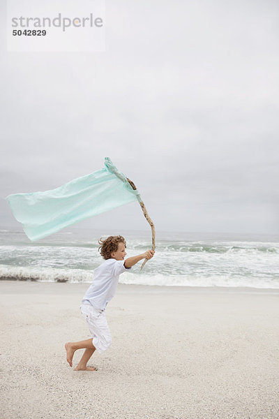 Junge läuft  während er die Fahne am Strand hält