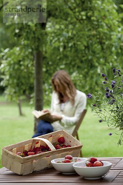 Erdbeeren auf dem Gartentisch  junge Frau liest im Hintergrund