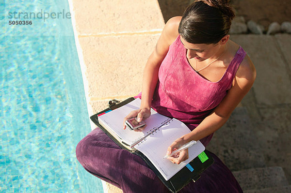 Frau am Schwimmbad mit Handy und Organizer