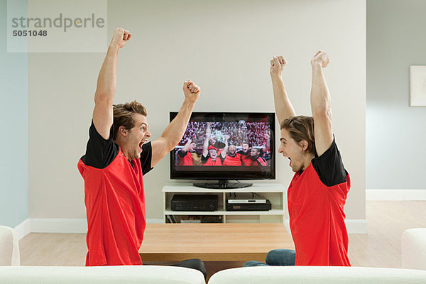 Zwei junge Männer in Fußballshirts beim Fußball schauen im Fernsehen