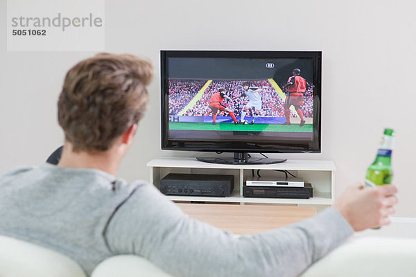 Junger Mann beim Fußball im Fernsehen mit Bierflasche