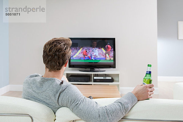 Junger Mann beim Fußball im Fernsehen mit Bierflasche