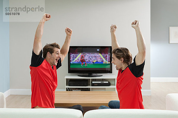 Zwei junge Männer in Fußballshirts beim Fußball schauen im Fernsehen