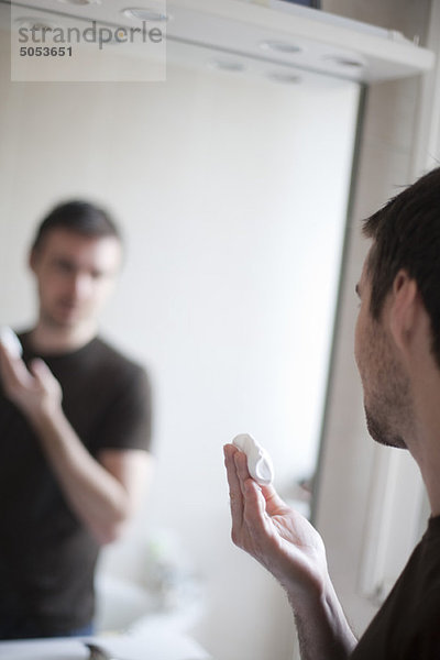 Mann schaut sich selbst im Spiegel an  Rasierschaum in der Hand