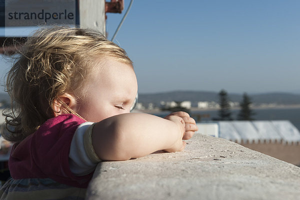 Kleinkind Mädchen lehnt sich mit geschlossenen Augen an die Seite des Balkons.
