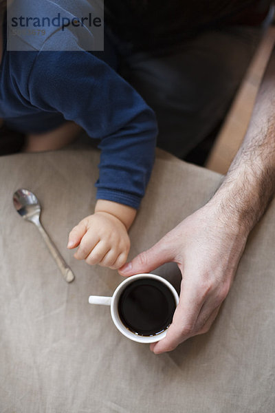 Mann  der eine Tasse Kaffee trinkt  während er Kleinkindesohn hält.