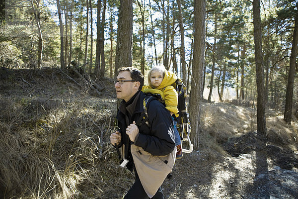 Vater Wandern im Wald mit Tochter im Rucksackträger