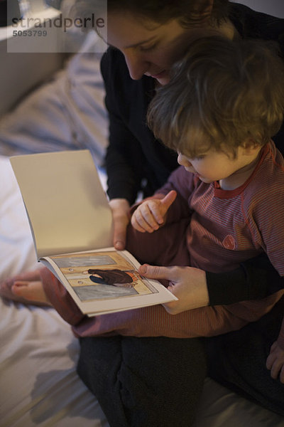 Mutter hält Kleinkind-Sohn auf Schoß  liest Gutenachtgeschichte