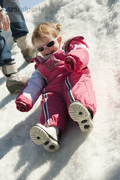 Kleinkind im Schneeanzug auf Schnee sitzend