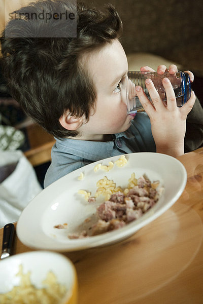 Kleiner Junge am Tisch  trinkt ein Glas Wasser.