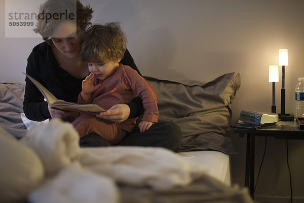 Mutter hält Kleinkind-Sohn auf dem Schoß  liest Gutenachtgeschichte im Bett