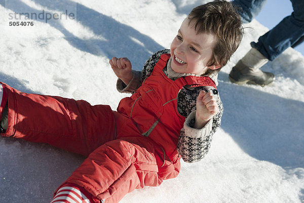 Junge im Schnee sitzend  lächelnd