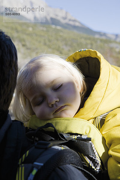 Kleines Mädchen schläft im Träger auf dem Rücken der Eltern