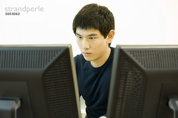 Junger Mann arbeitet am Computer mit zwei Monitoren