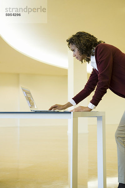 Geschäftsfrau  die sich gegen den Schreibtisch lehnt und einen Laptop benutzt.