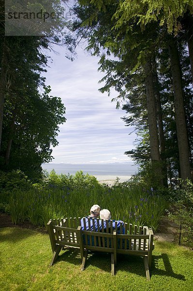 Ein senior Couple sitzen auf einer Bank auf dem Gelände am Milner Gärten & Wald  ein Garten am Meer inmitten natürlicher Küsten-Douglasie Wälder in Qualicum Beach  Vancouver Island  British Columbia  Kanada