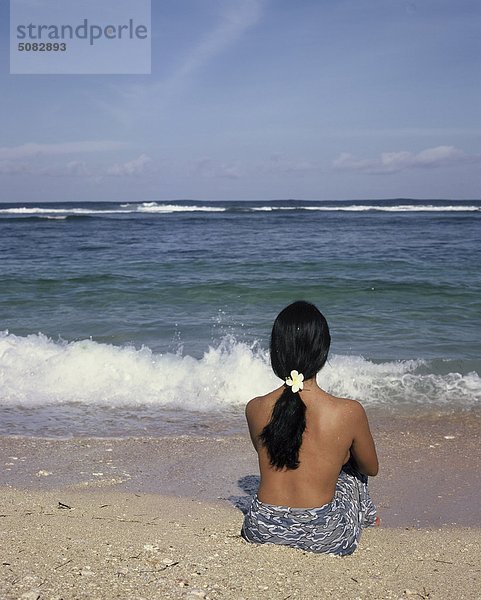 Frau sitzt am Strand  Rückansicht