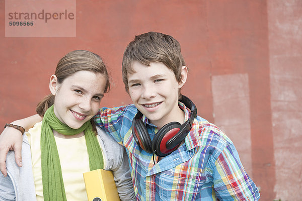 Lächelnder Junge mit Kopfhörer und Mädchen mit Mappe umarmen sich