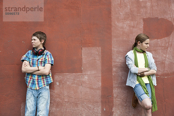 Junge mit Kopfhörer und Mädchen lehnen an einer Wand