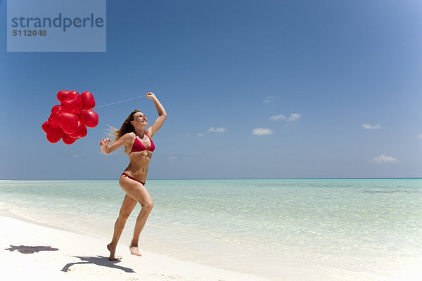 Frau läuft mit Luftballons am Strand