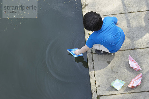 Junge spielt mit Papier-Segelbooten im Teich