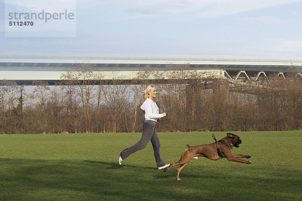 Frau läuft mit Hund im Feld
