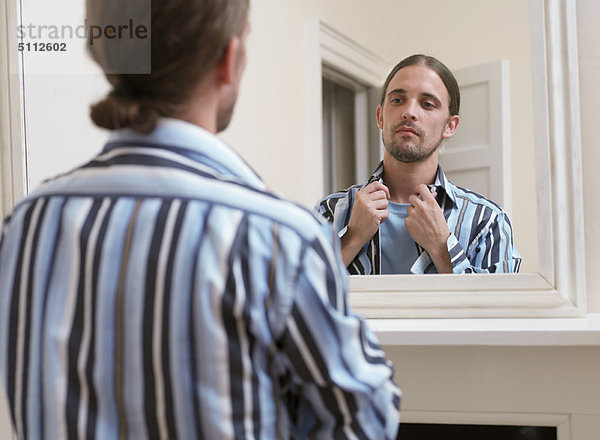 Mann stellt sein Hemd im Spiegel ein