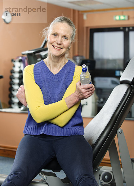 Ältere Frau trinkt Wasser im Fitnessstudio